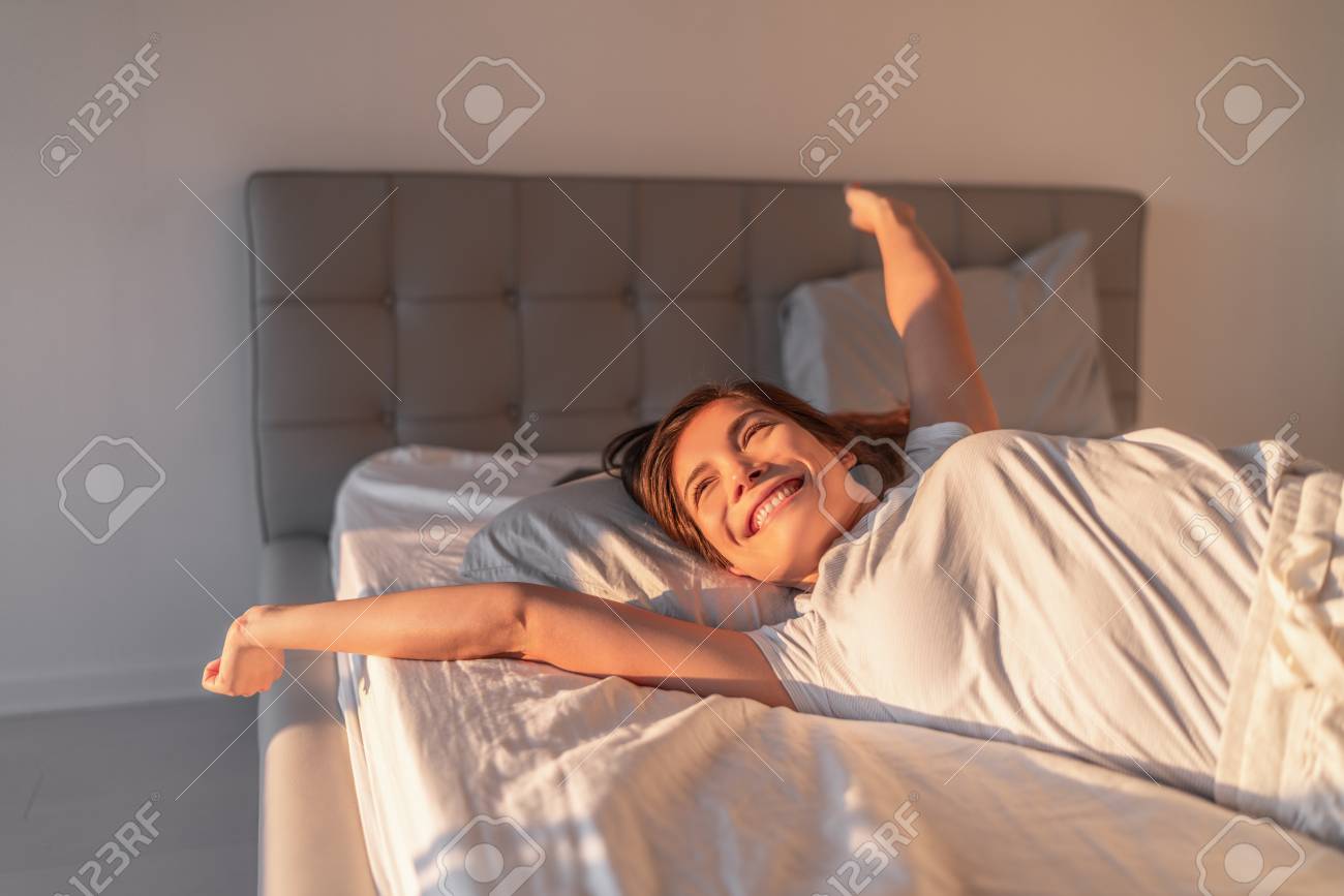 Happy girl waking up in the morning sunshine looking at sunrise sun in window excited to enjoy the day. Wake up energetic Asian woman lying in bed well rested from a good night sleep. - 118452235 Happy girl waking up in the morning sunshine looking at sunrise sun in window excited to enjoy the day. Wake up energetic Asian woman lying in bed well rested from a good night sleep. - 118452235