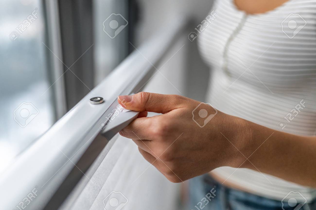 TOP-DOWN BOTTOM-UP WINDOW SHADES. Woman raising cellular shade blind at home from the lower to the top of windows. - 122804488 TOP-DOWN BOTTOM-UP WINDOW SHADES. Woman raising cellular shade blind at home from the lower to the top of windows. - 122804488