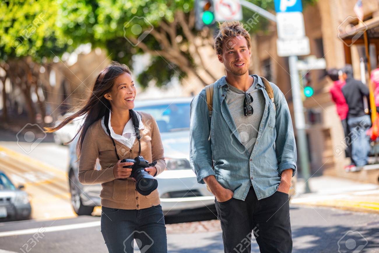 Young students couple tourists walking in city street taking photos with camera on travel. Asian woman, Caucasian man friends urban lifestyle casual. - 122804552 Young students couple tourists walking in city street taking photos with camera on travel. Asian woman, Caucasian man friends urban lifestyle casual. - 122804552