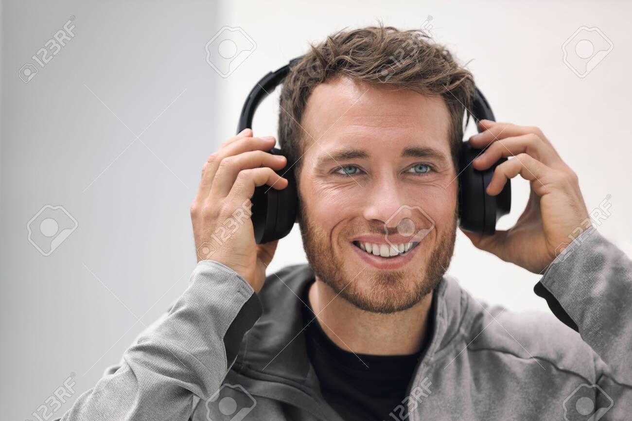Music headphones man listening to audiobook online or songs on phone app. Happy smiling young person wearing wireless earphones. Young adult buying techonology wearable device at store. - 139907454 Music headphones man listening to audiobook online or songs on phone app. Happy smiling young person wearing wireless earphones. Young adult buying techonology wearable device at store. - 139907454
