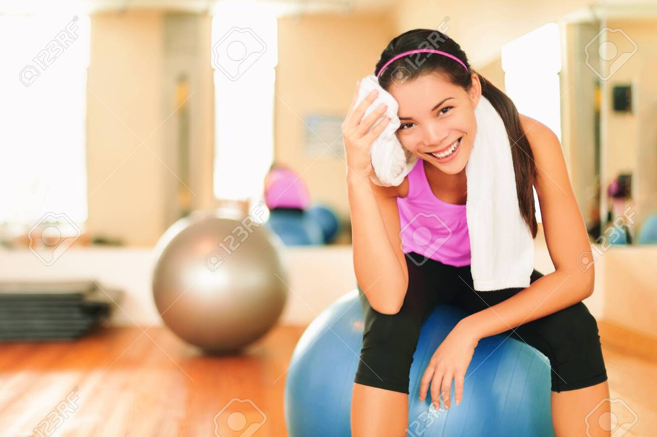 Asian fitness girl training at gym wiping sweat with towel post workout happy at gym. Exercise and healthy living weight loss concept. - 154450133 Asian fitness girl training at gym wiping sweat with towel post workout happy at gym. Exercise and healthy living weight loss concept. - 154450133