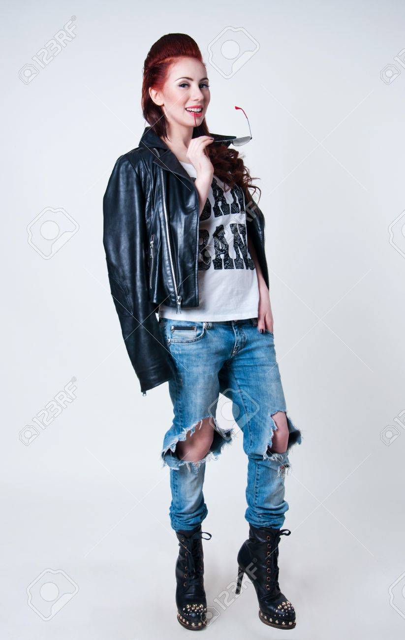 Mooie jonge rocker vrouw model met schattige rode kapsel, draagt ​​lederen jas, spijkerbroek geript, zwarte laarzen met hoge hakken en spikes, met Mooie jonge rocker vrouw model met schattige rode kapsel, draagt ​​lederen jas, spijkerbroek geript, zwarte laarzen met hoge hakken en spikes, met
