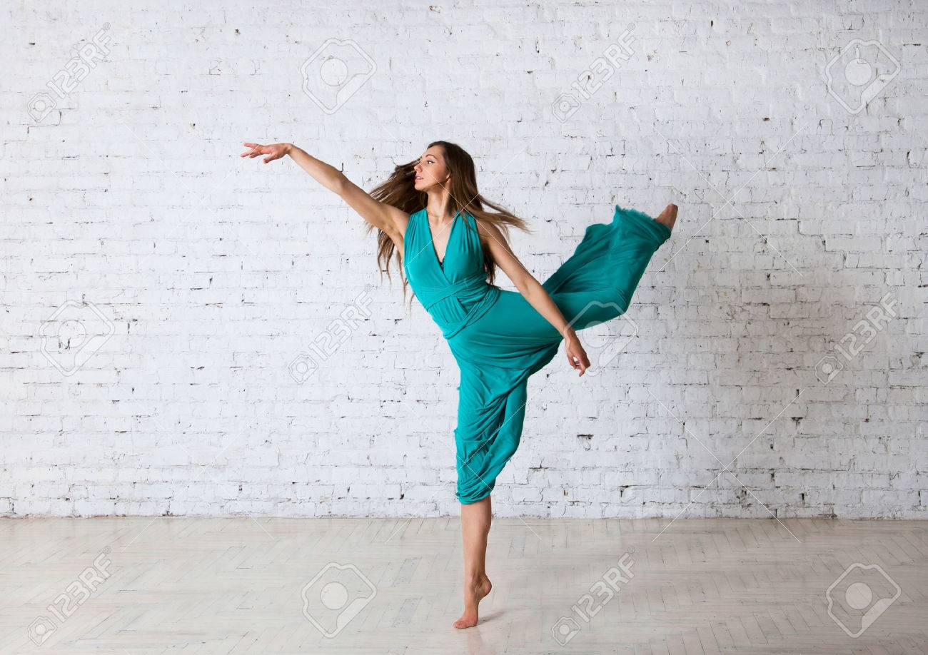 若い美しい女性ダンサーのピルエット やっているポーズ ダンス スタジオでジャンプ つま先 彼女青いターコイズ ロングドレス カーテンに入る空気で髪 Flyong で立っています レンガ壁の背景の上 の写真素材 画像素材 Image