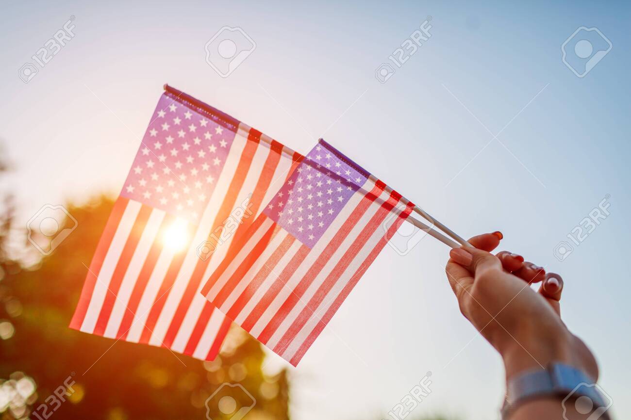 Woman holding USA flag against the blue sky. Celebrating Independence Day of America - 125426995 Woman holding USA flag against the blue sky. Celebrating Independence Day of America - 125426995