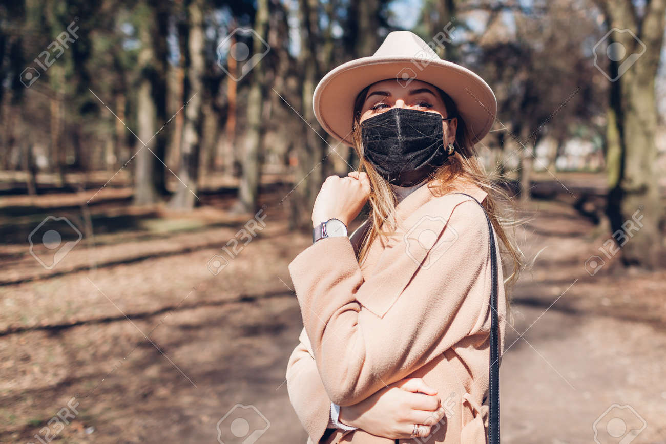 Stylish woman wears reusable mask outdoors during coronavirus covid-19 pandemic in empty spring park. - 168610567 Stylish woman wears reusable mask outdoors during coronavirus covid-19 pandemic in empty spring park. - 168610567