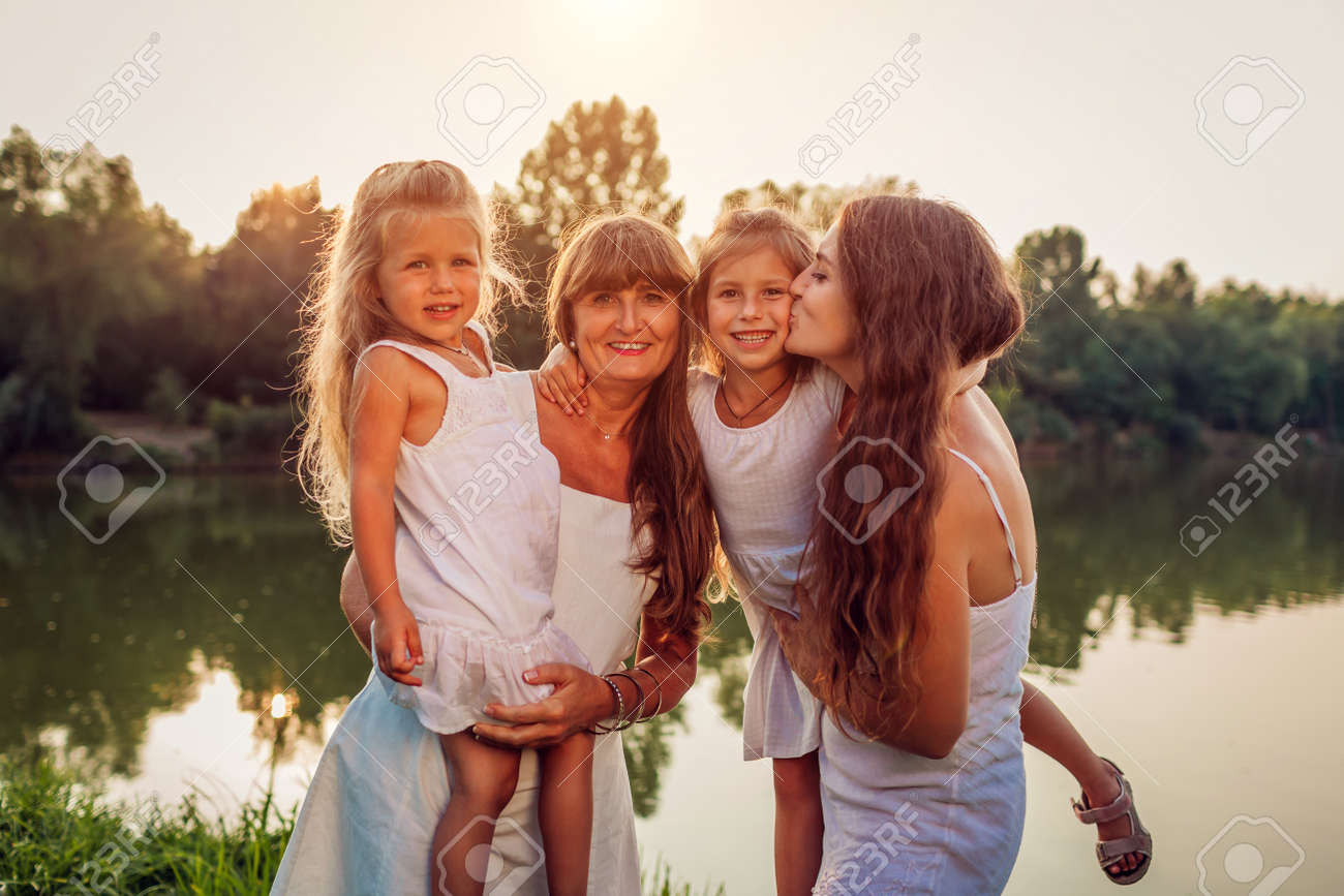 Women's day. Family walking by summer river at sunset. Mother and grandmother holding daughters kids. Three denerations. Girls having fun - 168610504 Women's day. Family walking by summer river at sunset. Mother and grandmother holding daughters kids. Three denerations. Girls having fun - 168610504