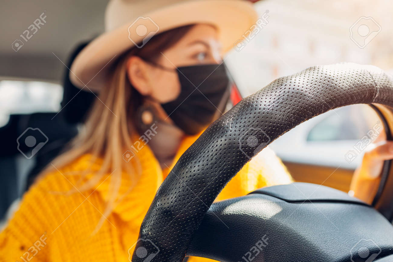 Stylish woman driving car wearing protective mask during coronavirus covid-19 pandemic. Safety measures. Close up of steering wheel - 168610471 Stylish woman driving car wearing protective mask during coronavirus covid-19 pandemic. Safety measures. Close up of steering wheel - 168610471