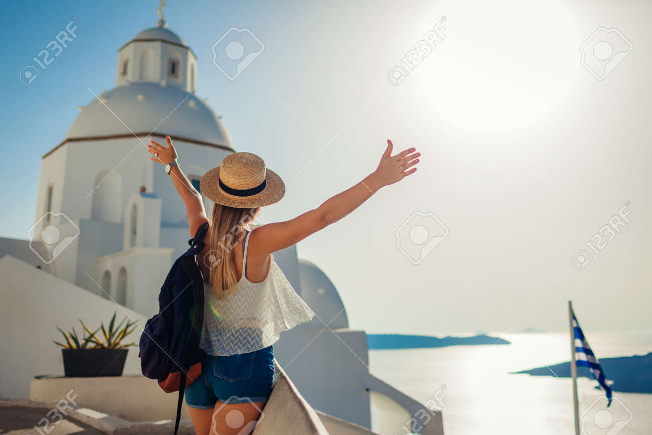 Woman tourist raised arms looking at Caldera sea landscape in Fira, Santorini island walking by traditional church. - 171282234 Woman tourist raised arms looking at Caldera sea landscape in Fira, Santorini island walking by traditional church. - 171282234