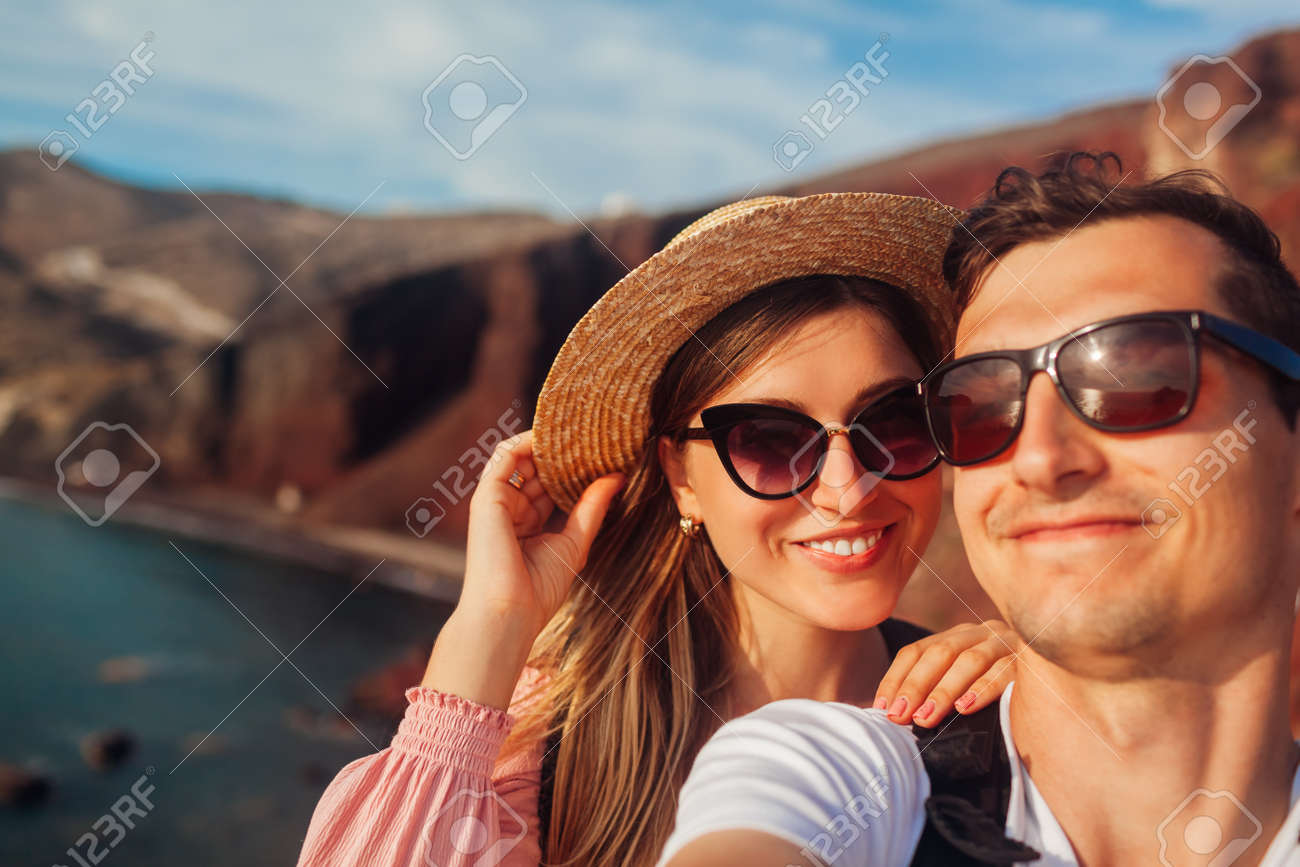 Loving couple takes selfie enjoying honeymoon on Red beach on Santorini island, Greece. Summer vacation. Traveling - 171513221 Loving couple takes selfie enjoying honeymoon on Red beach on Santorini island, Greece. Summer vacation. Traveling - 171513221