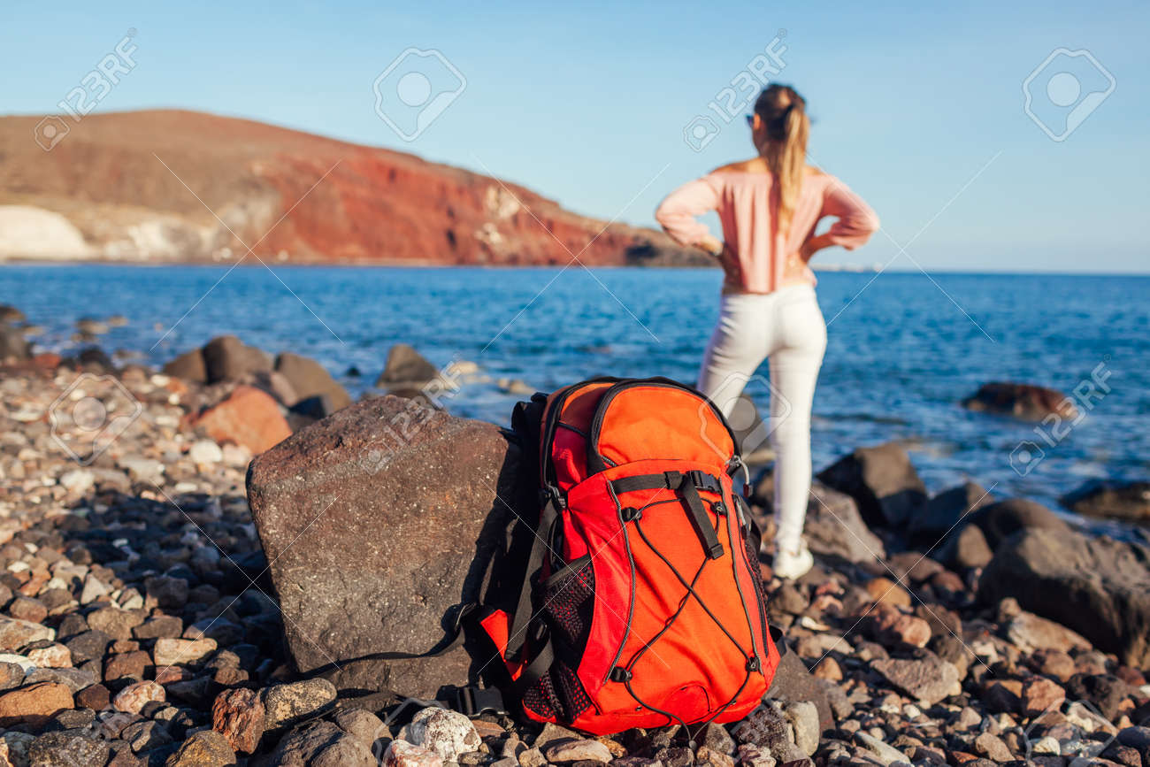 Hiker woman with backpack walking on Red beach on Santorini island, Greece enjoying sea and mountain landscape. Traveling and summer vacation - 171513199 Hiker woman with backpack walking on Red beach on Santorini island, Greece enjoying sea and mountain landscape. Traveling and summer vacation - 171513199