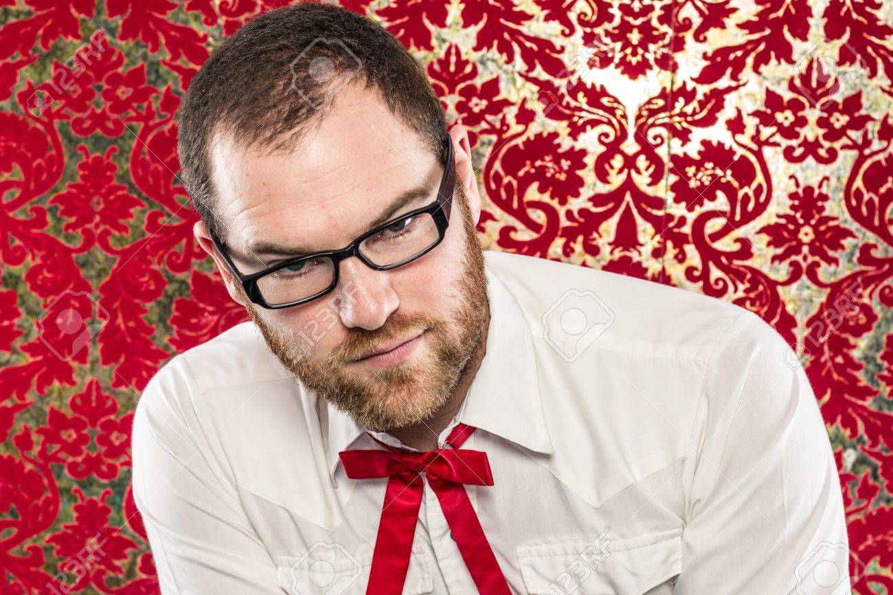 ブラック フレーム眼鏡をかけている男 白いシャツ 赤いテキサス ネクタイ ビンテージ赤い壁紙引き摺り下ろさ自信を持ってカメラを見ながら前に座っています の写真素材 画像素材 Image