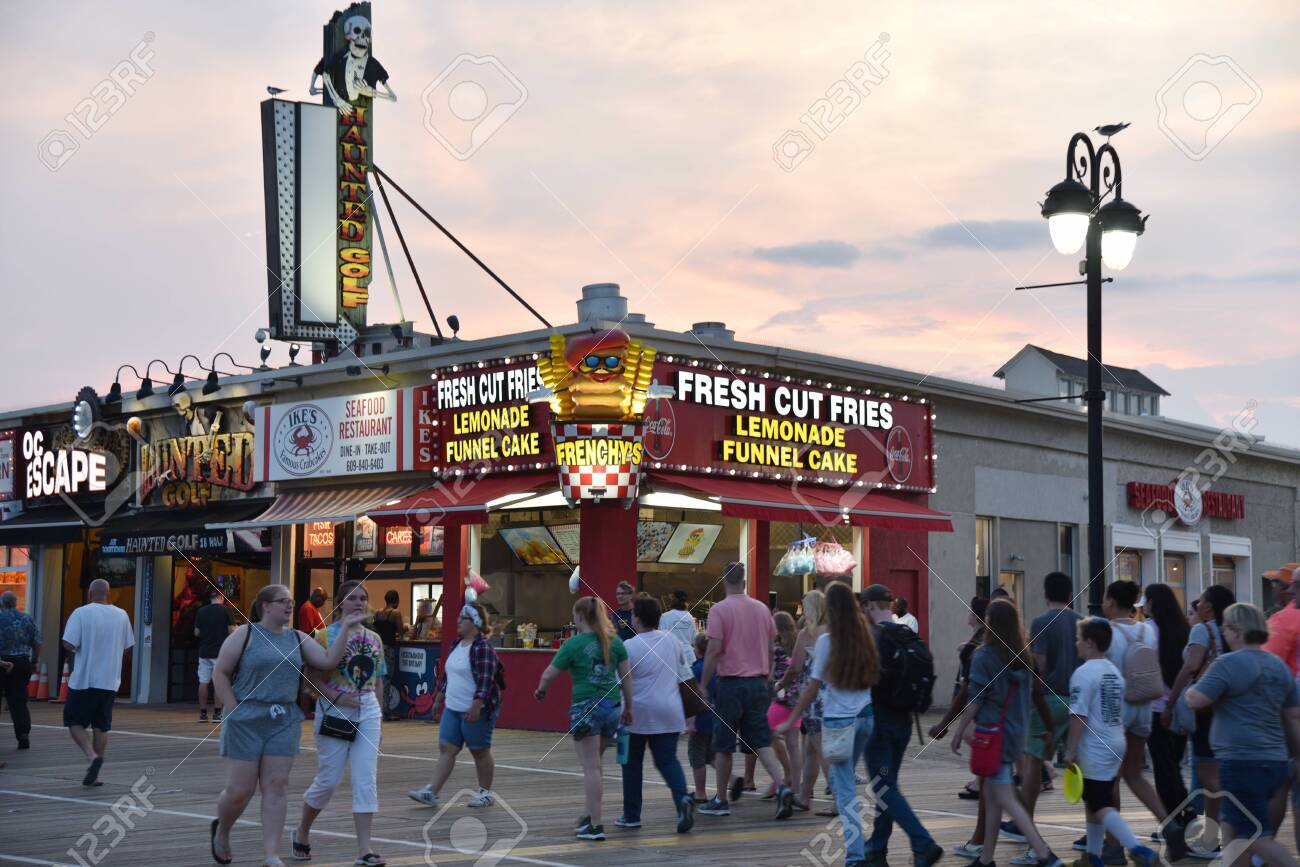 OCEAN CITY, NEW JERSEY/USA - JUNE 27, 2019: Tourists passing food stands and amusement arcades on the Ocean City Boardwalk at sunset - 136575794 OCEAN CITY, NEW JERSEY/USA - JUNE 27, 2019: Tourists passing food stands and amusement arcades on the Ocean City Boardwalk at sunset - 136575794