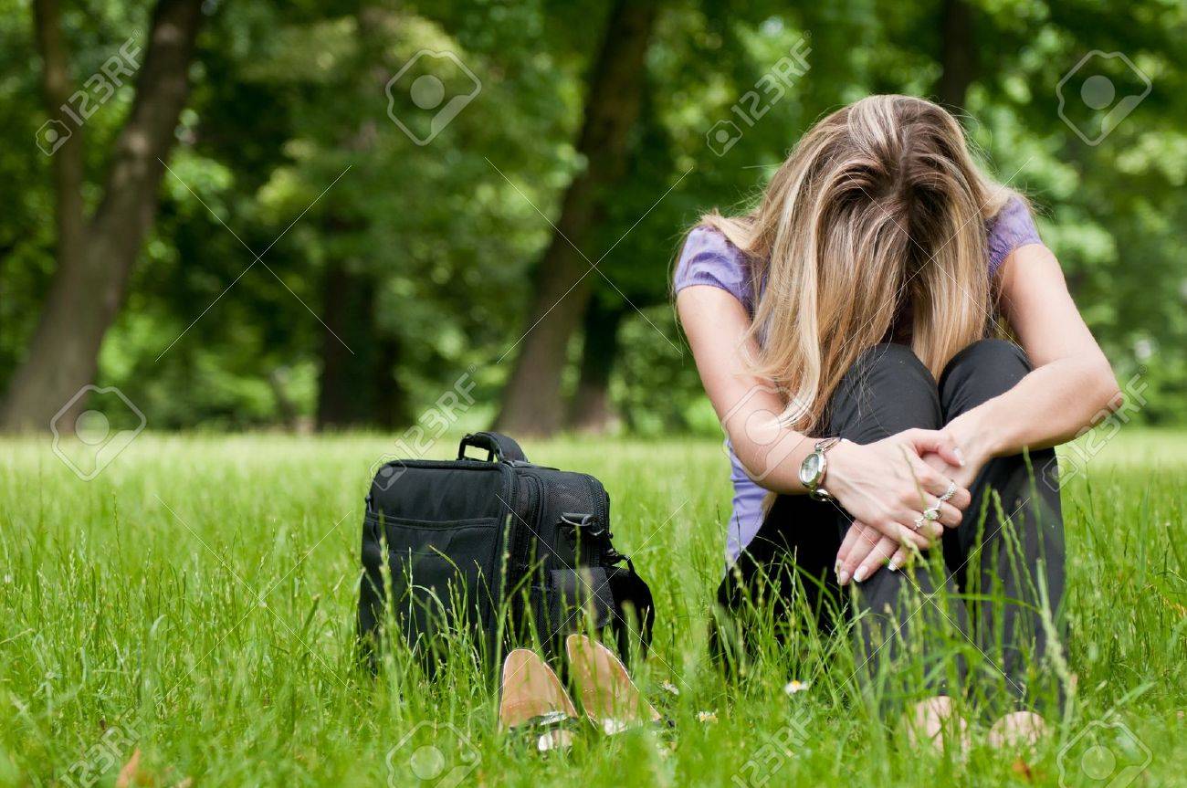 Young depressed business woman siting in grass - notebook bag and shoes lying next - 7201637 Young depressed business woman siting in grass - notebook bag and shoes lying next - 7201637