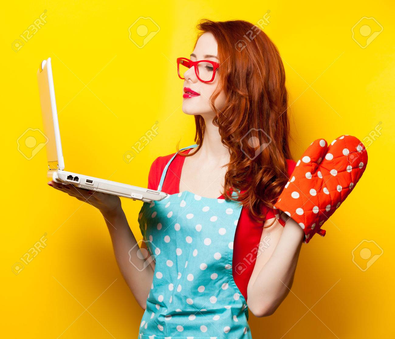 Young housewife with computer and oven gloves on yellow background - 37324370 Young housewife with computer and oven gloves on yellow background - 37324370