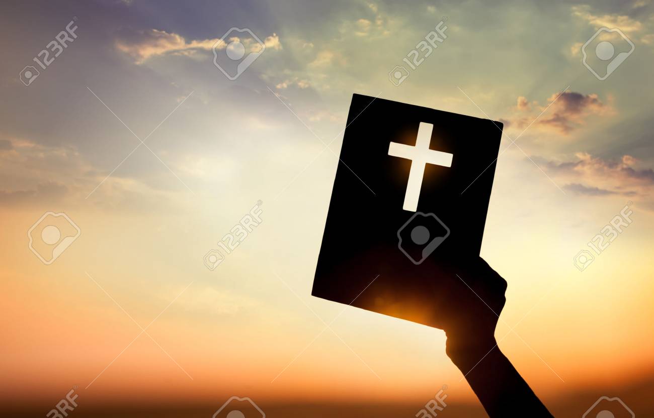 Hand holding book with cross on sunset background - 37470922 Hand holding book with cross on sunset background - 37470922