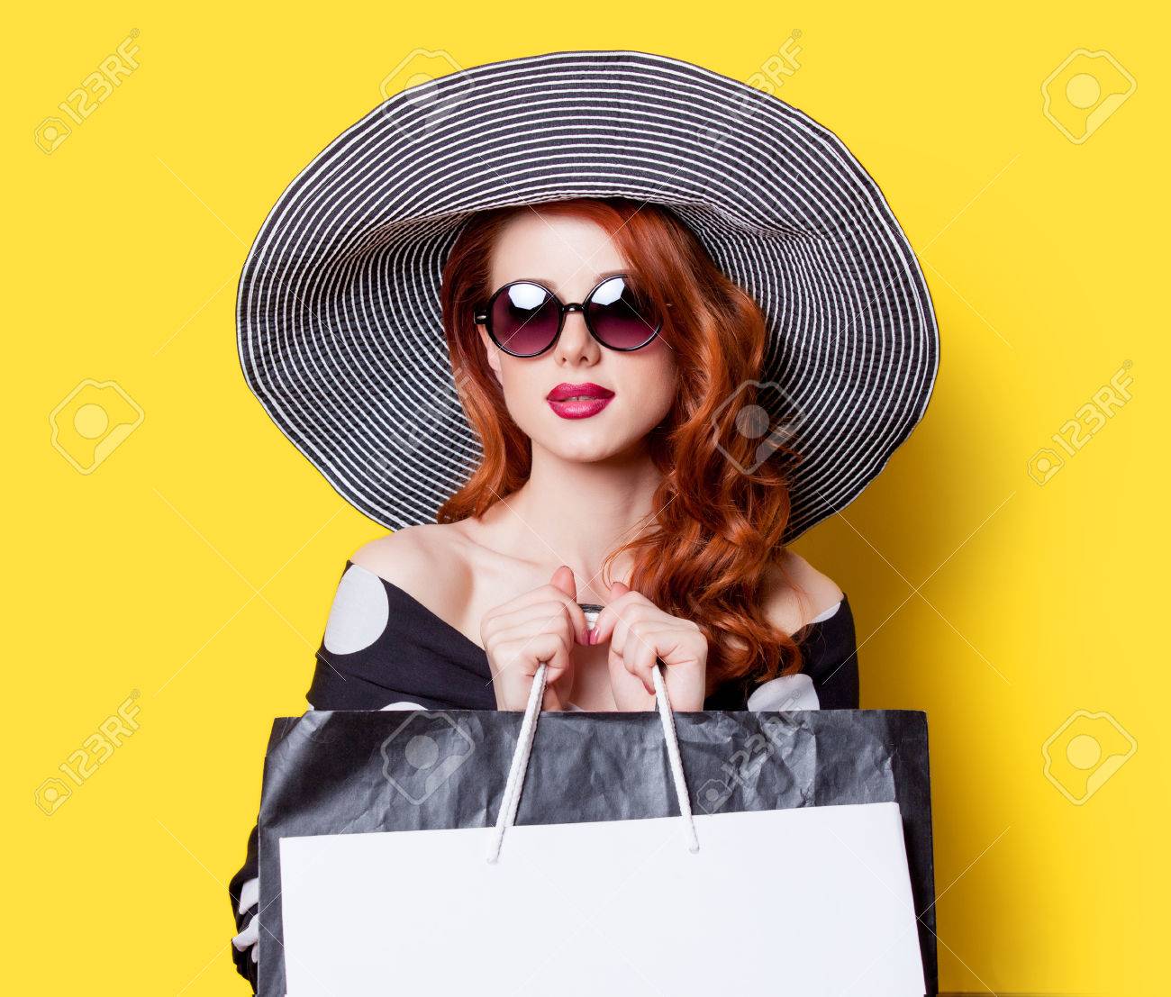 Redhead girl in black dress and hat with shopping bags on yellow background - 40455213 Redhead girl in black dress and hat with shopping bags on yellow background - 40455213