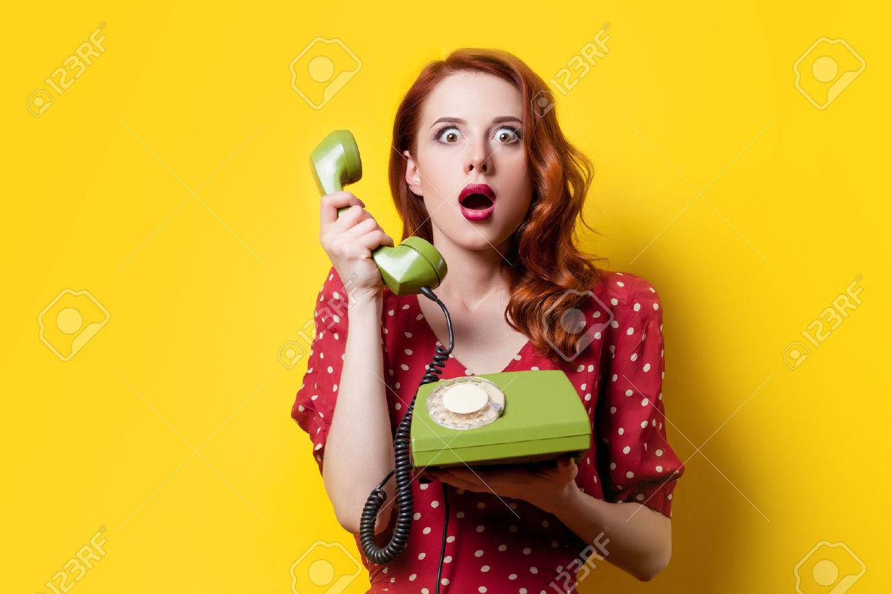 Surprised redhead girl in red polka dot dress with green dial phone on yellow background. - 40455220 Surprised redhead girl in red polka dot dress with green dial phone on yellow background. - 40455220