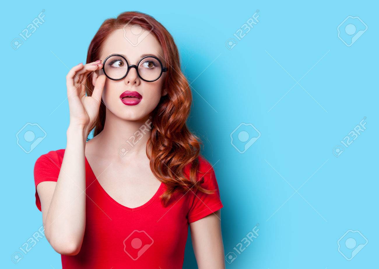 Surprised redhead girl in red dress with glasses on blue background - 40455101 Surprised redhead girl in red dress with glasses on blue background - 40455101