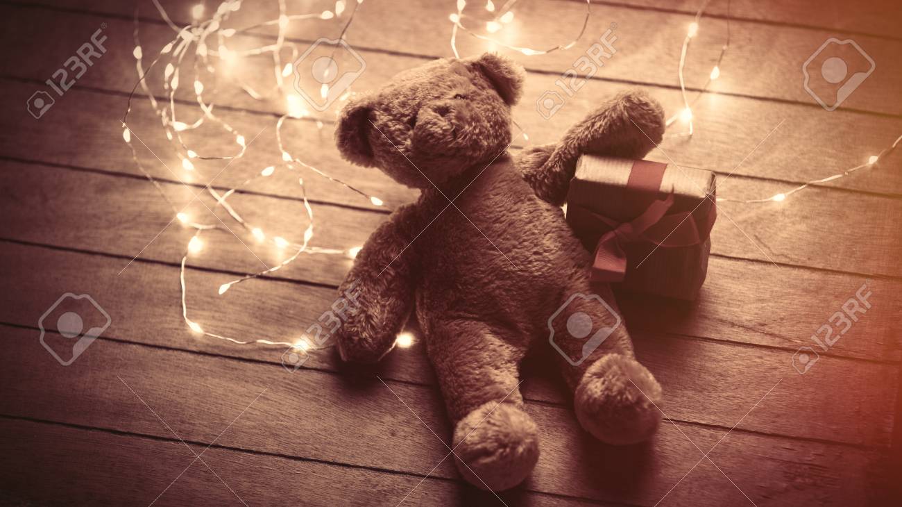 ギフトや素敵な茶色の木製の背景に明るいガーランドを持つかわいいふわふわのテディベア の写真素材 画像素材 Image