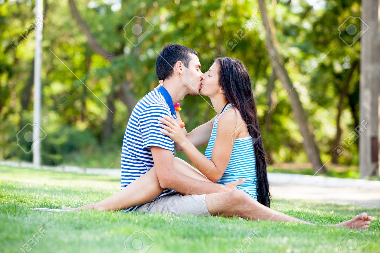 photo of cute couple sitting and kissing on the grass on the stock