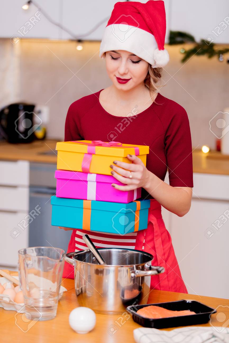 Young Housewife With Christmas Gifts Cooking Dinner In The Kitchen