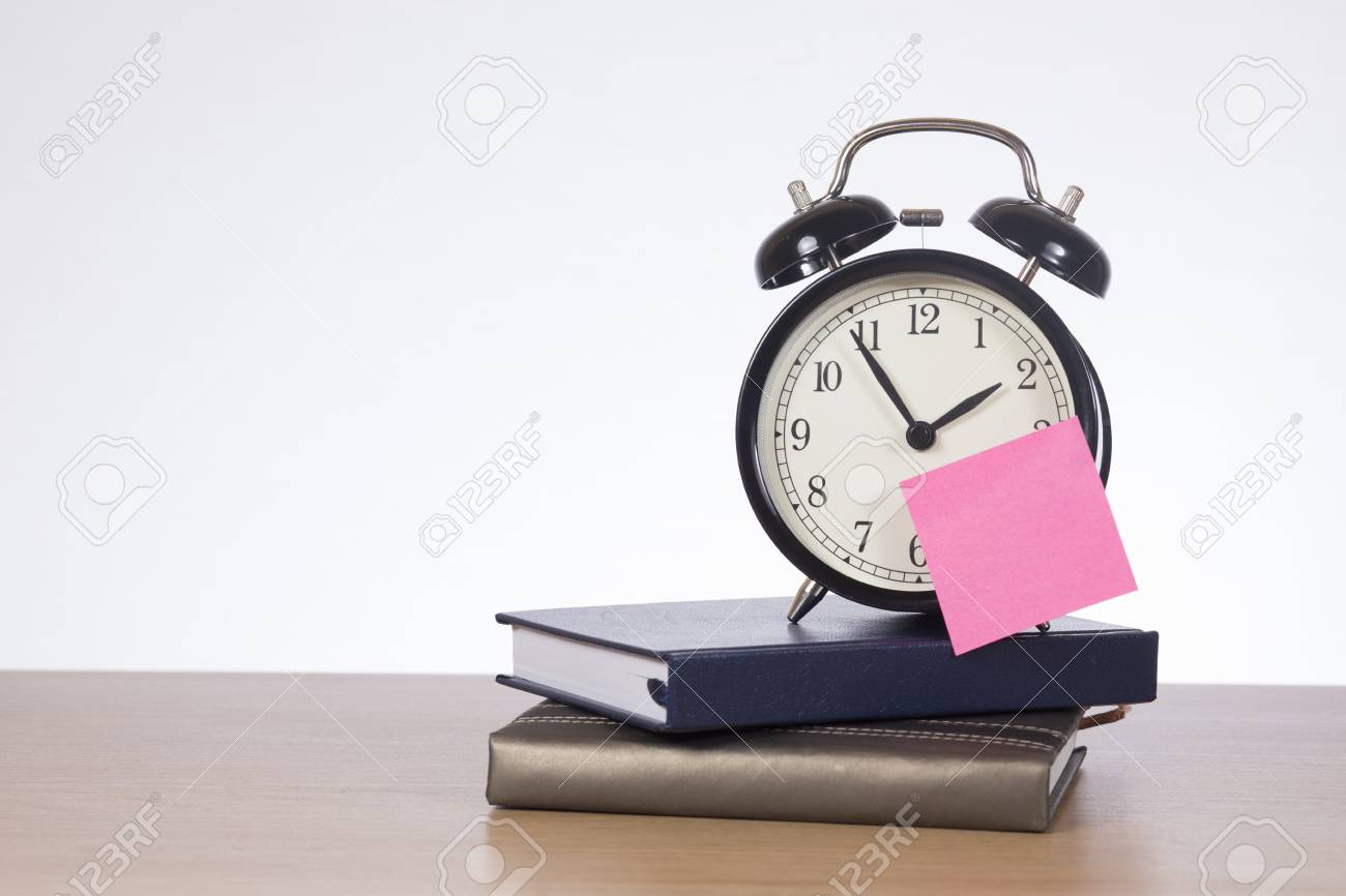 alarm clock with sticky note standing on pile of calendars on pictures of calendars