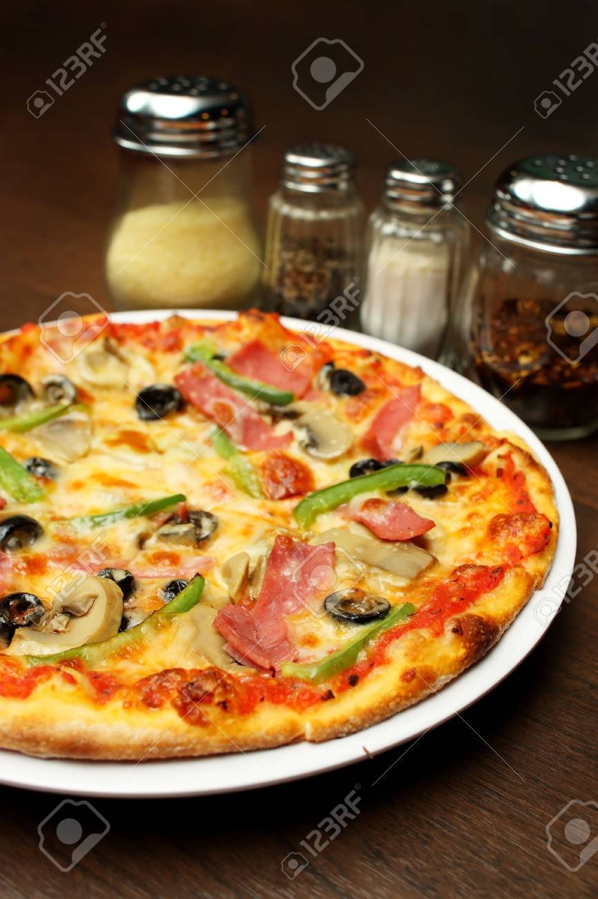 Close up of a pizza with seasoning on brown table. - 4627796 Close up of a pizza with seasoning on brown table. - 4627796