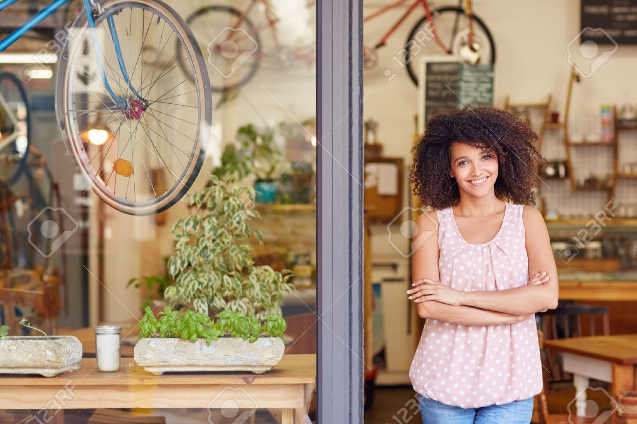 Young mixed race woman smiling, while standing in the door of her cafe with her arms folded proud to be the owner of a small business - 51356645 Young mixed race woman smiling, while standing in the door of her cafe with her arms folded proud to be the owner of a small business - 51356645