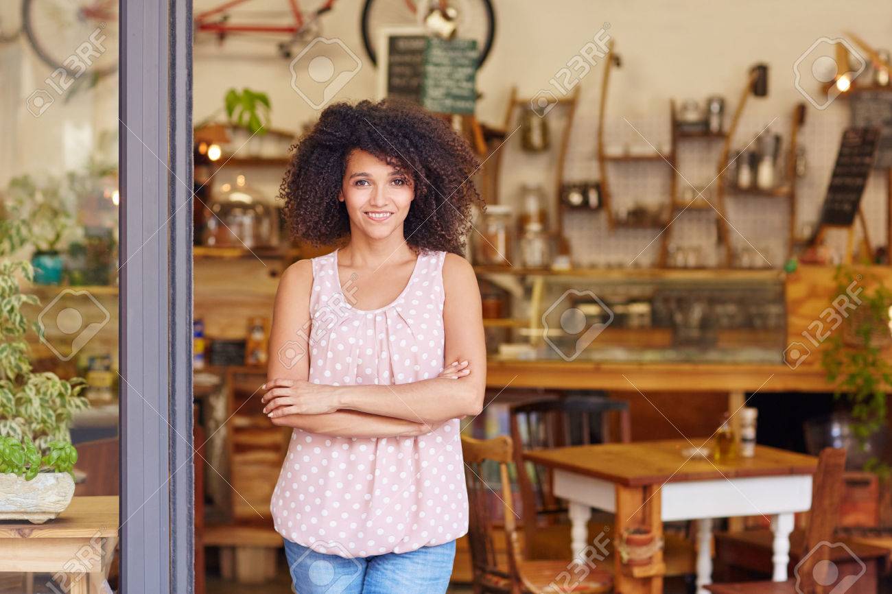 Beautiful young cafe owner proud of her small business standing smiling in the doorway of her coffee shop - 51356646 Beautiful young cafe owner proud of her small business standing smiling in the doorway of her coffee shop - 51356646