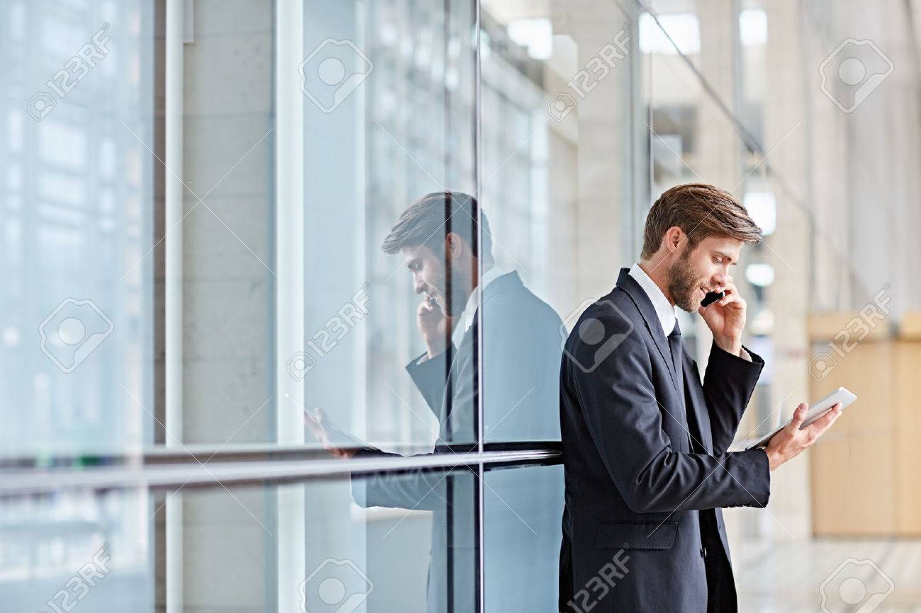 Corporate executive smiling while talking on his phone and looking at a digital tablet - 51813595 Corporate executive smiling while talking on his phone and looking at a digital tablet - 51813595