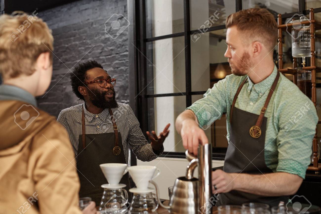 African Man Managing A Modern Coffee Shop Explaining The Process To New Barista Who Is African Man Managing A Modern Coffee Shop Explaining The Process To New Barista Who Is