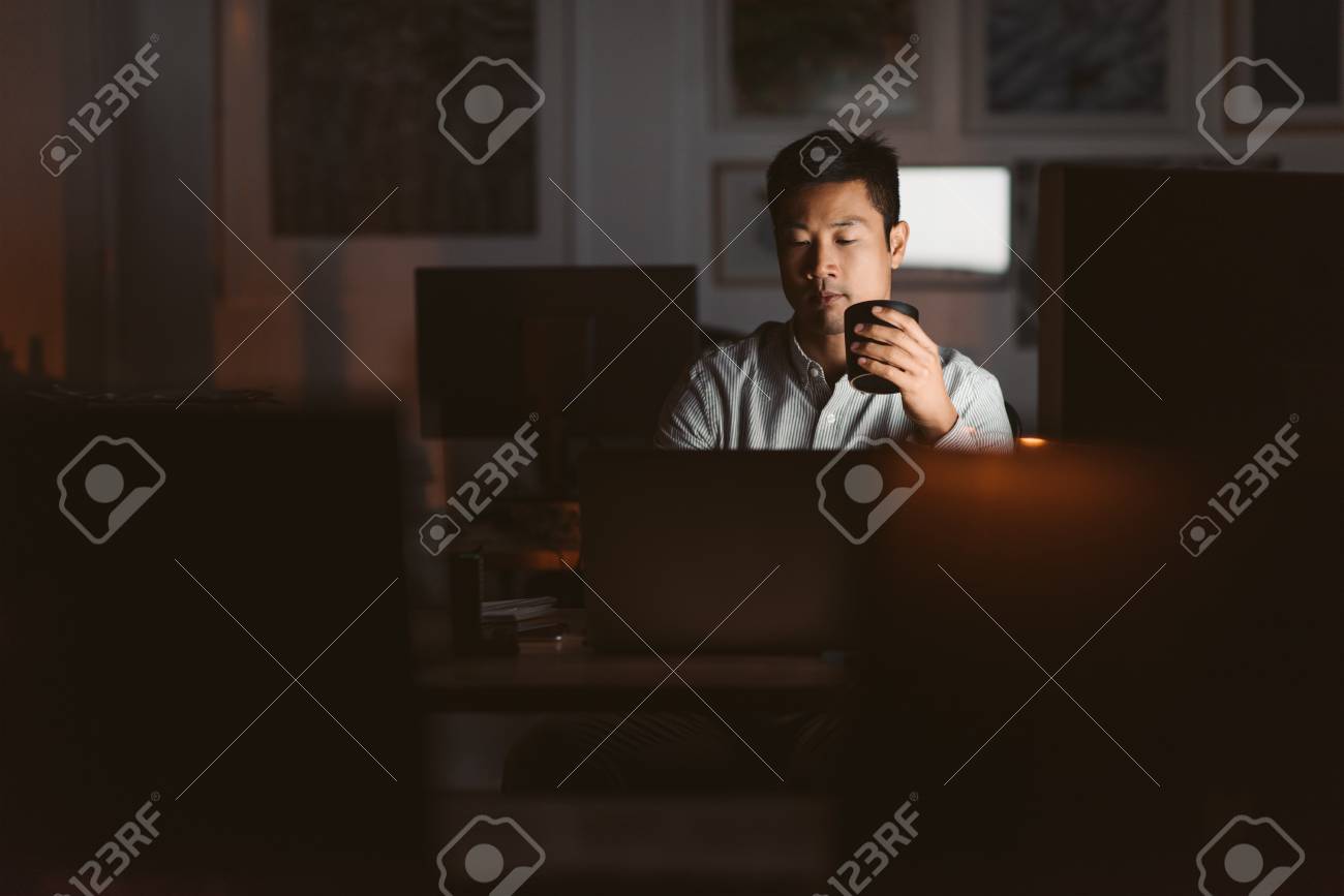 Asian businessman drinking coffee while working late in an offic - 108839402 Asian businessman drinking coffee while working late in an offic - 108839402