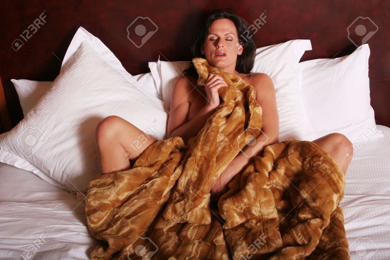 Mature woman in bed, fur blanket partially covering her curves, eyes closed in sensual repose