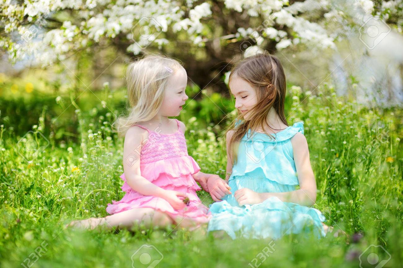 Two Cute Little Sisters Sitting On The Grass In Blooming Cherry.. Stock Photo, Picture And Royalty Free Image. Image 41693281.