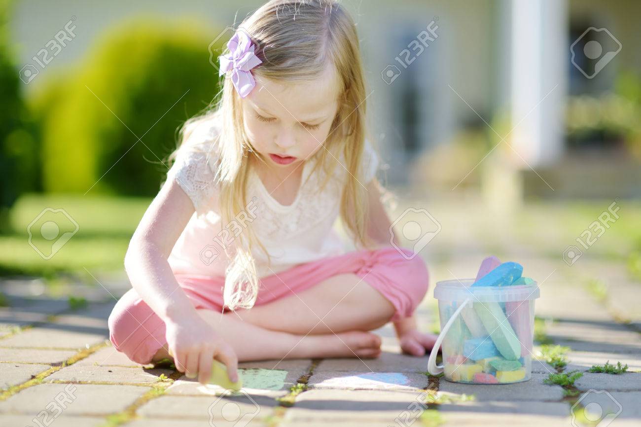 Cute Little Girl Drawing With Colorful Chalks On A Sidewalk
