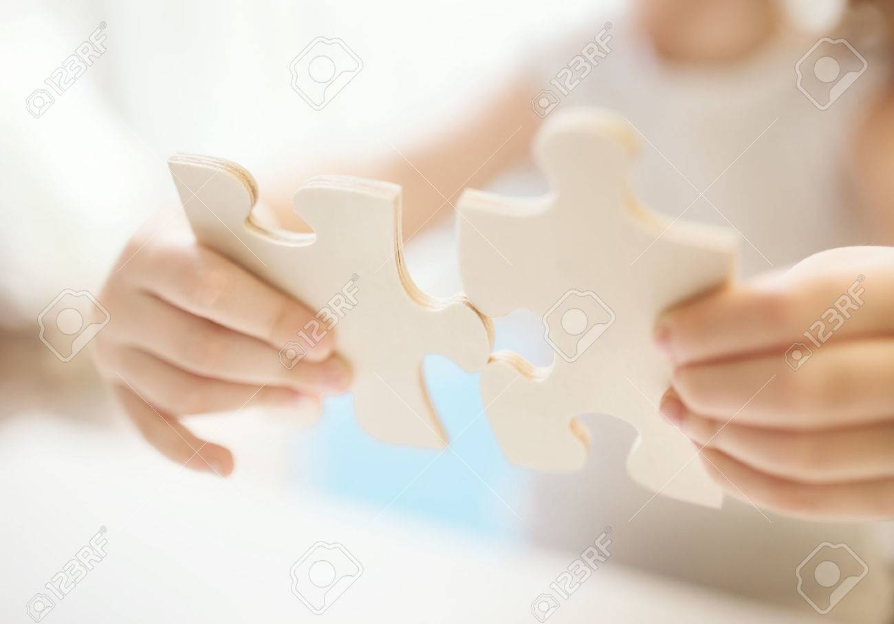 child girl holding two big wooden puzzle pieces hands connecting