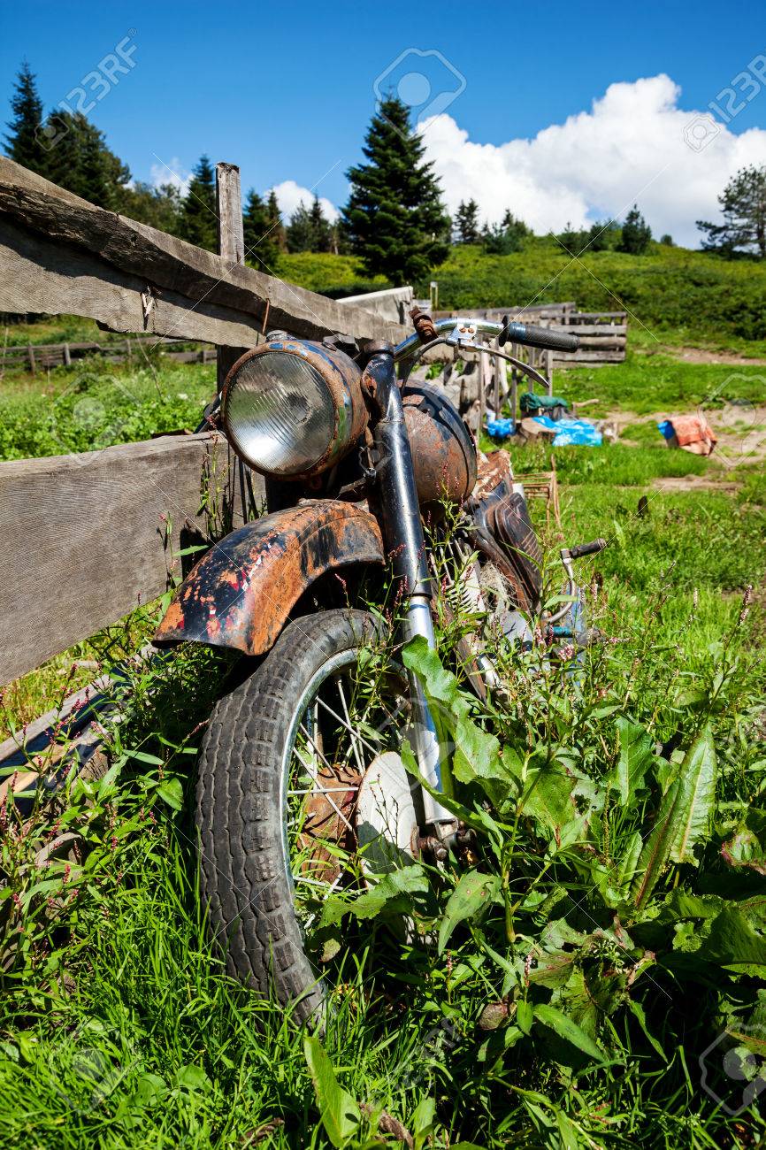村の地方で古いバイクを断念しました。フェンスの近くの草を草に覆われ ...