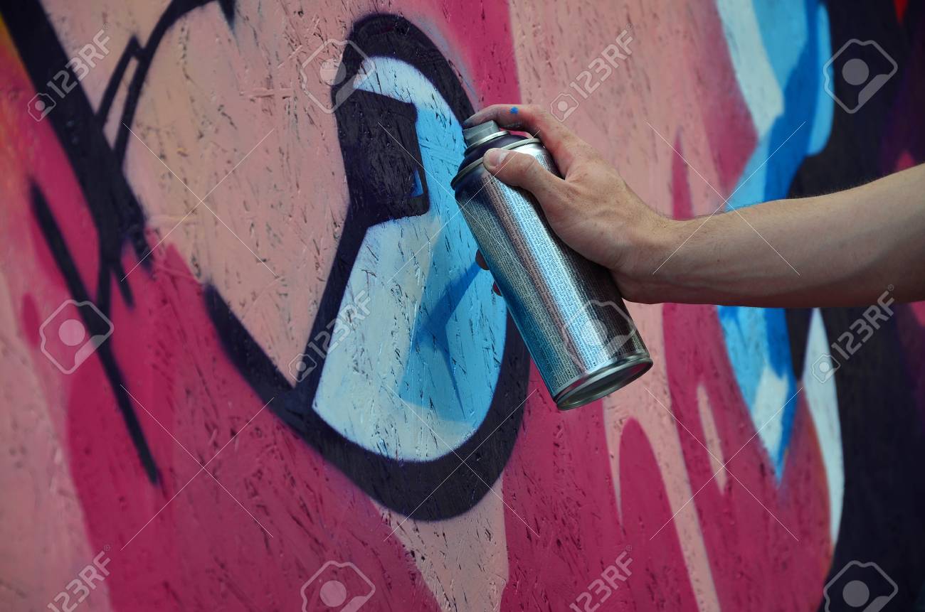 壁に新しい落書きを描くスプレー缶を持つ手。木製の壁クローズアップに