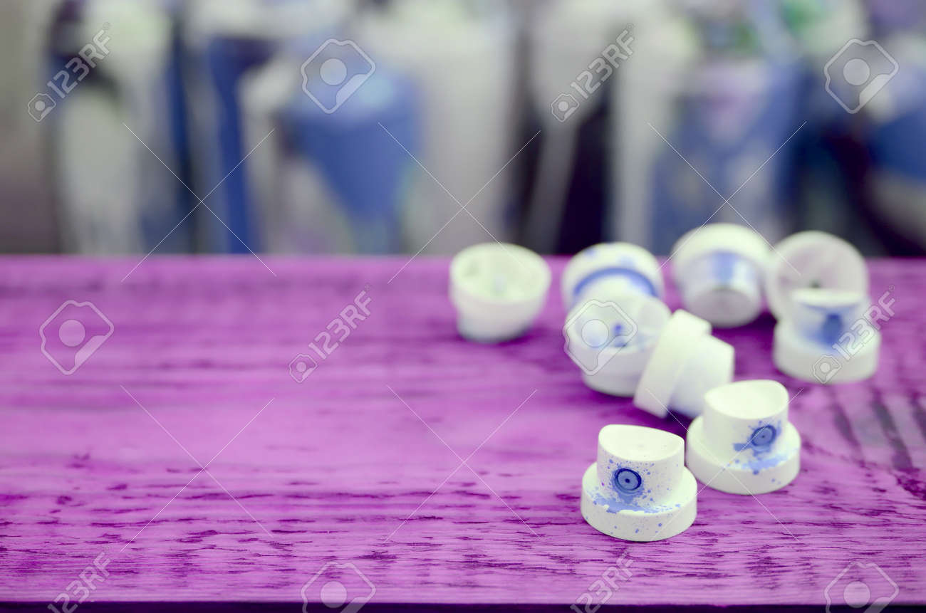 The soiled blue nozzles from the paint sprayer lies on a purple plank on a background of a many dirty spray cans for graffiti painting - 167450173 The soiled blue nozzles from the paint sprayer lies on a purple plank on a background of a many dirty spray cans for graffiti painting - 167450173