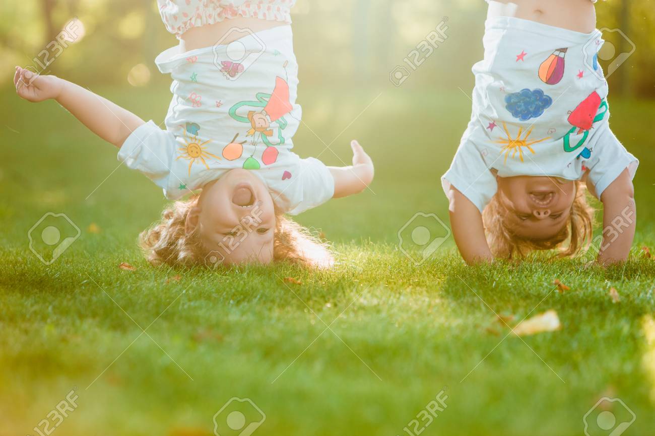 2 年の古い緑の草に対して逆さまにぶら下がっている 2 つの小さな赤ちゃん女の子 の写真素材 画像素材 Image