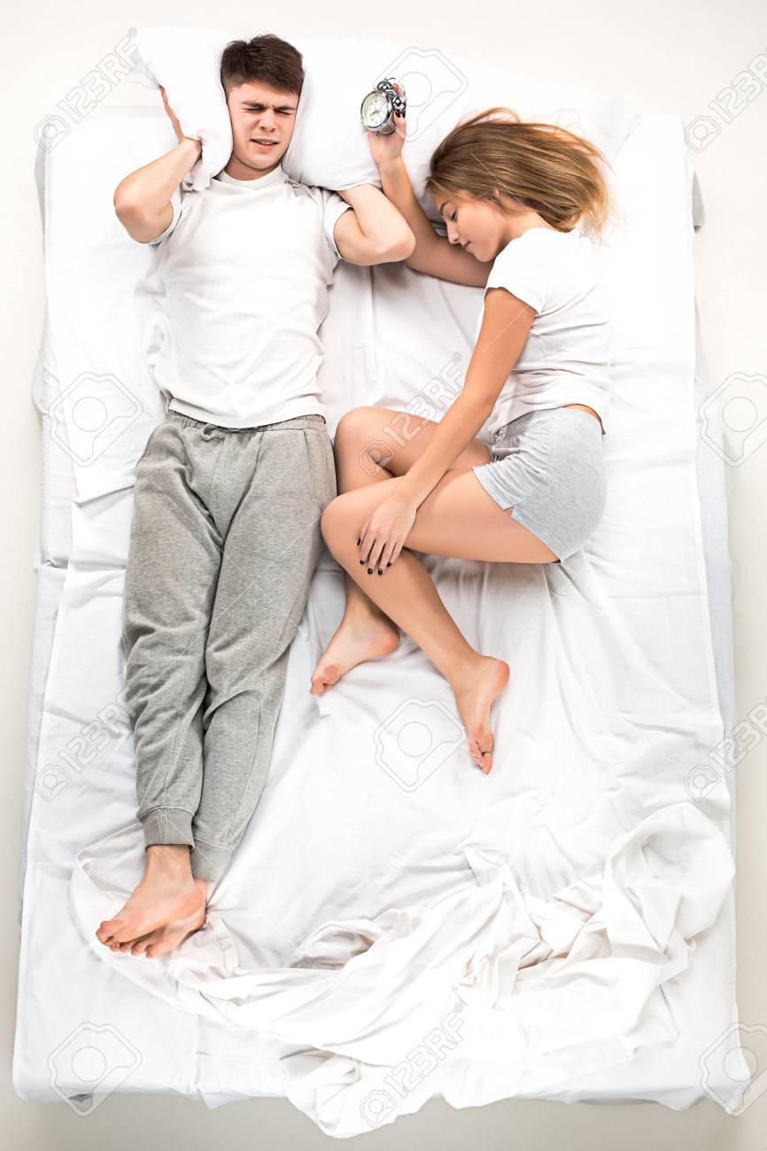 The Young Lovely Couple Lying In A White Bed With Alarm Clock