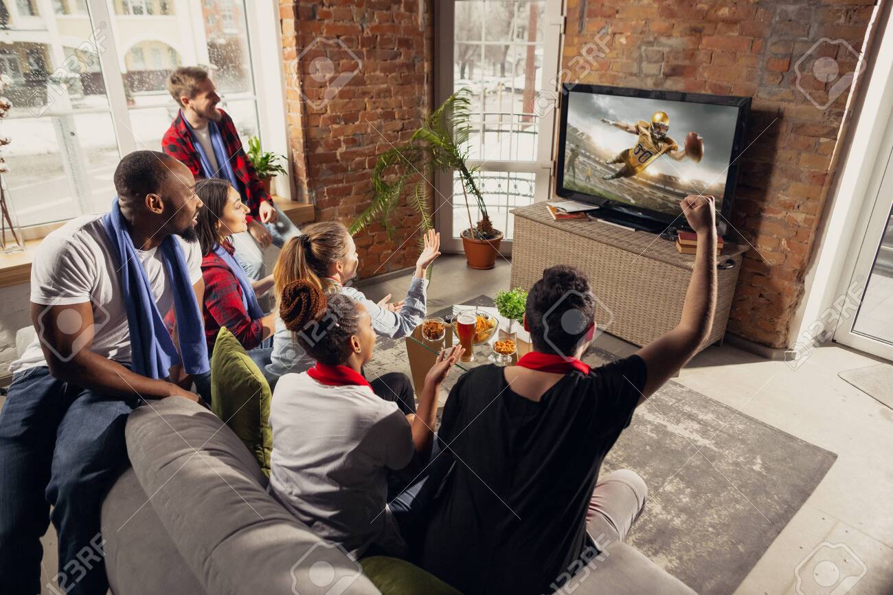 Excited group of people watching american football, sport match at home. Multiethnic group of emotional friend, fans cheering for favourite national team, drinking beer. Concept of emotions, support. - 141084947 Excited group of people watching american football, sport match at home. Multiethnic group of emotional friend, fans cheering for favourite national team, drinking beer. Concept of emotions, support. - 141084947