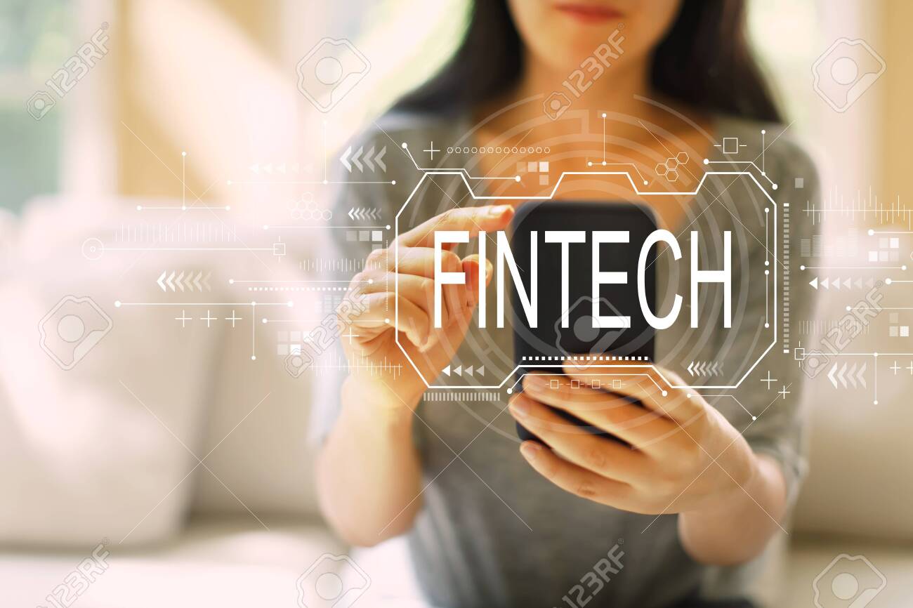 Fintech concept with woman using her smartphone in a living room - 121429299 Fintech concept with woman using her smartphone in a living room - 121429299