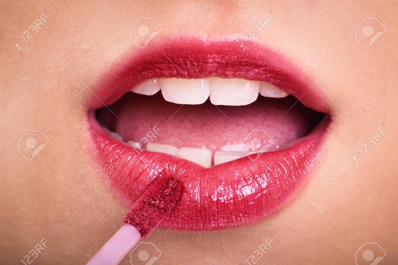 Cosmetics, makeup and skin care concept. Close up of woman applying lipstick or lip gloss to her plump pink lips. - 142659128 Cosmetics, makeup and skin care concept. Close up of woman applying lipstick or lip gloss to her plump pink lips. - 142659128
