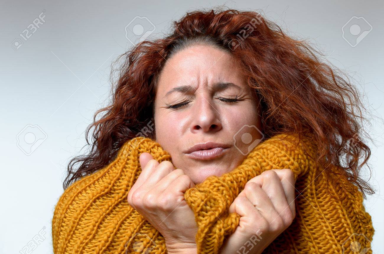 Cold young woman snuggling into a warm knitted woollen winter top with a grimace and her eyes closed as she tries to warm up, close up on white - 67102150 Cold young woman snuggling into a warm knitted woollen winter top with a grimace and her eyes closed as she tries to warm up, close up on white - 67102150