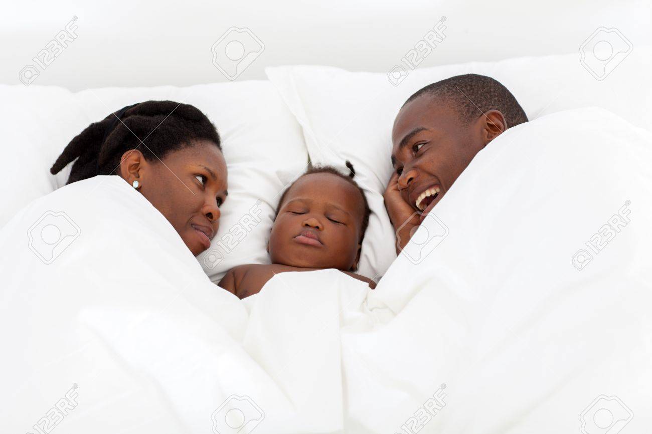 Heureux Couple Afro Americain Parlant Sur Le Lit Avec Le Bebe A Dormir Milieu Banque D Images Et Photos Libres De Droits Image