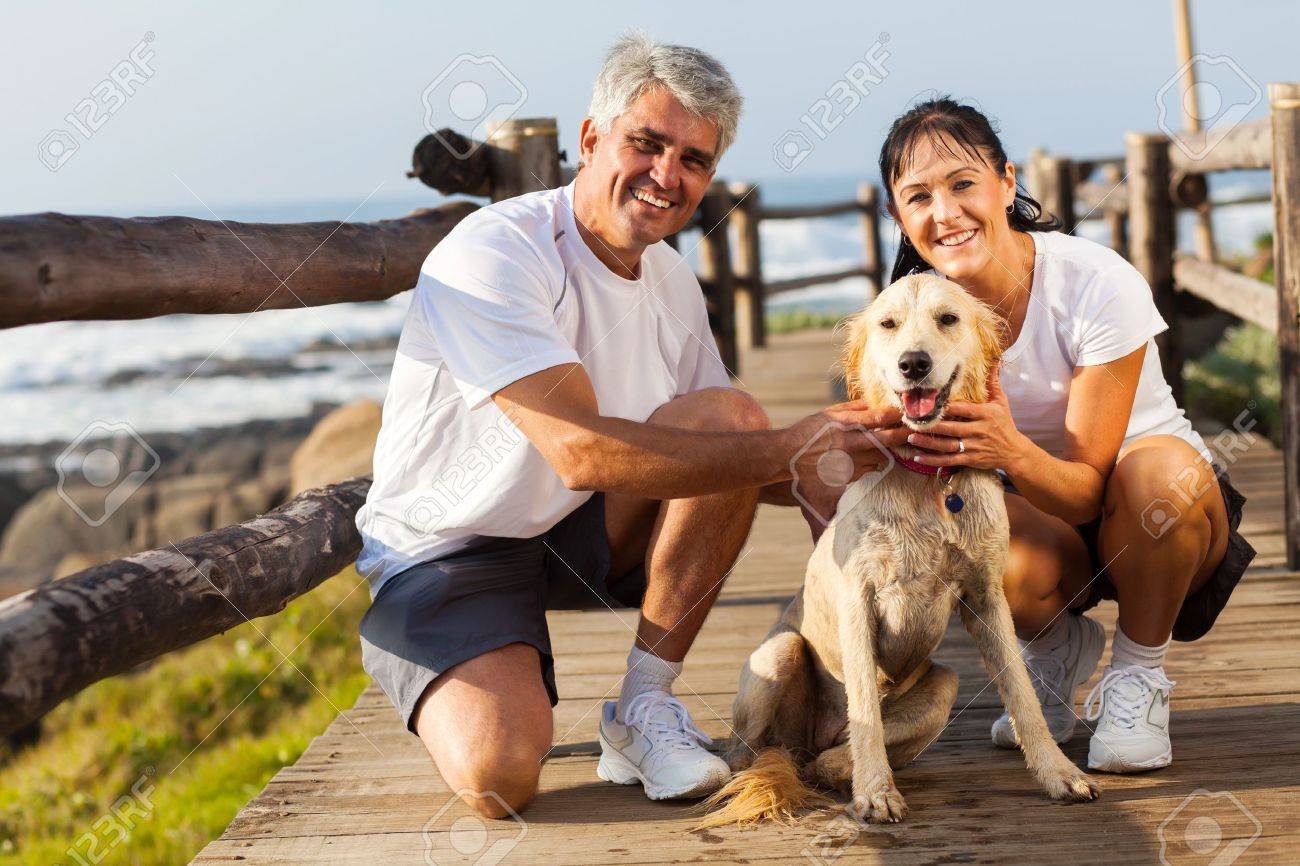スポーティな中年夫婦と午前中にビーチでのペットの犬 の写真素材 画像素材 Image