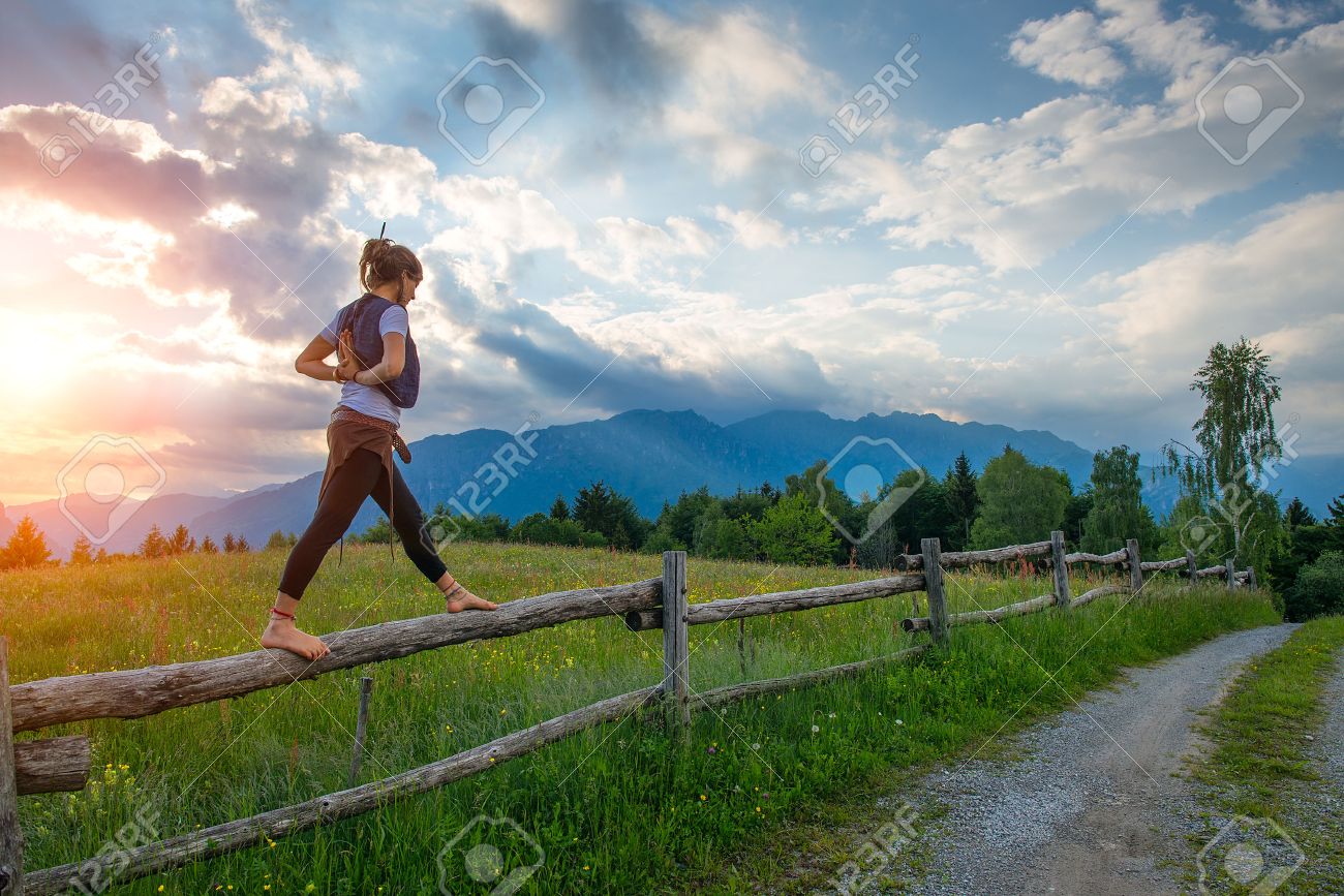Casual girl relaxes doing stretching and yoga alone in the mountains over a fence in a beautiful spring meadow. - 44574667 Casual girl relaxes doing stretching and yoga alone in the mountains over a fence in a beautiful spring meadow. - 44574667