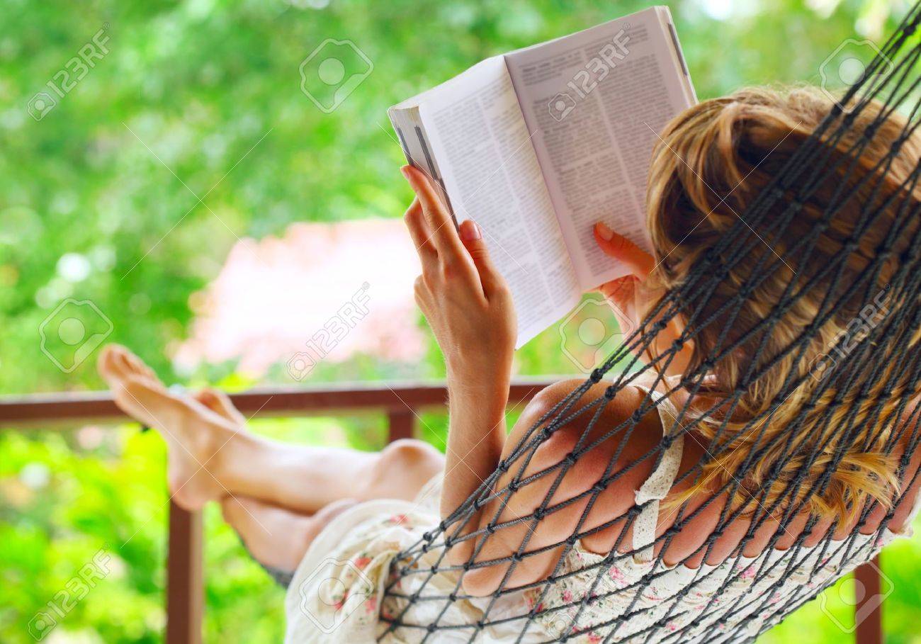 Young woman lying in hammock in a garden and reading a book. Shallow DOF. Focus on a left shoulder - 9912221 Young woman lying in hammock in a garden and reading a book. Shallow DOF. Focus on a left shoulder - 9912221
