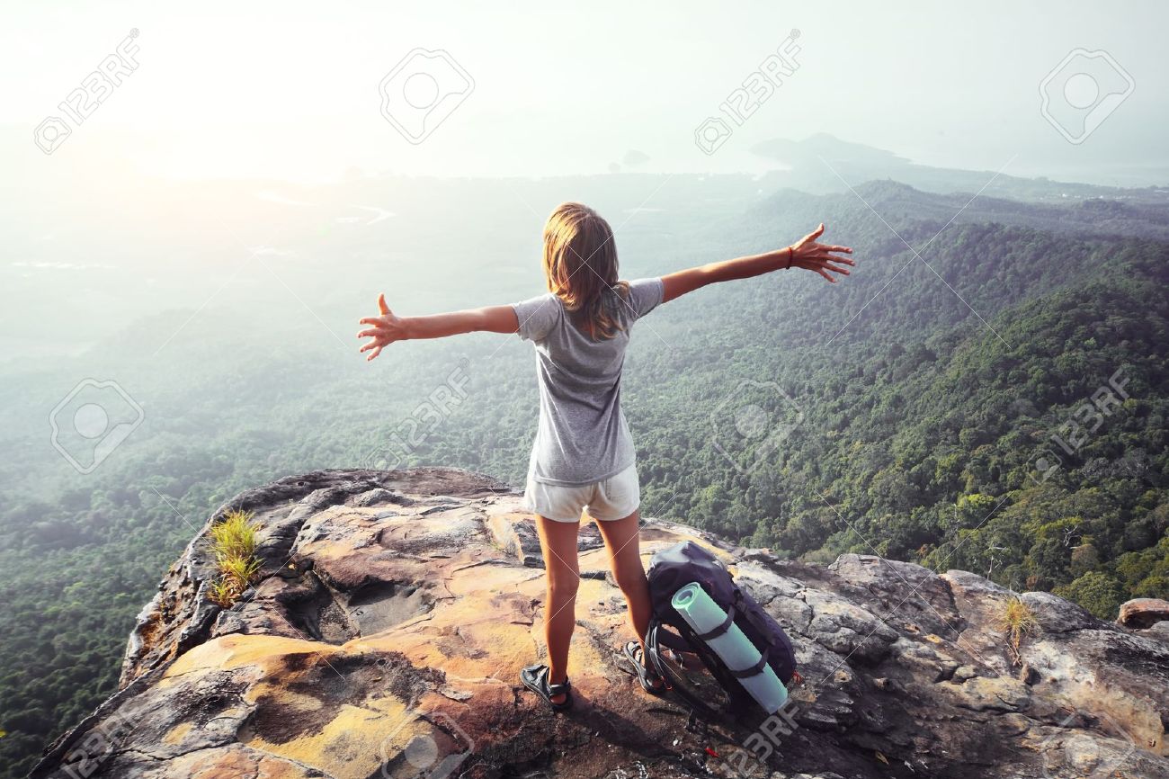 Young Woman Standing With Raised Hands Backpack On Cliffs Edge And Looking Into A Wide Young Woman Standing With Raised Hands Backpack On Cliffs Edge And Looking Into A Wide